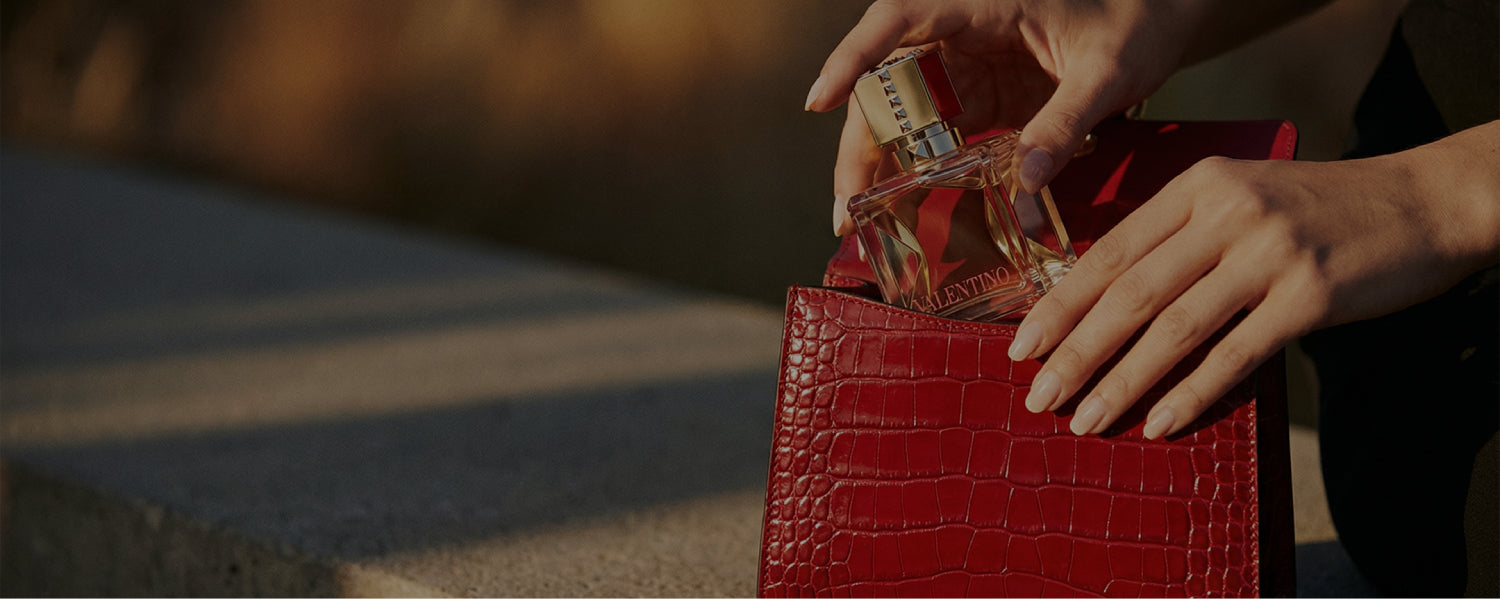 Red handbag with a hand holding a perfume bottle against a blurred background