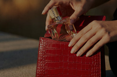 Hand placing a perfume bottle into a red handbag